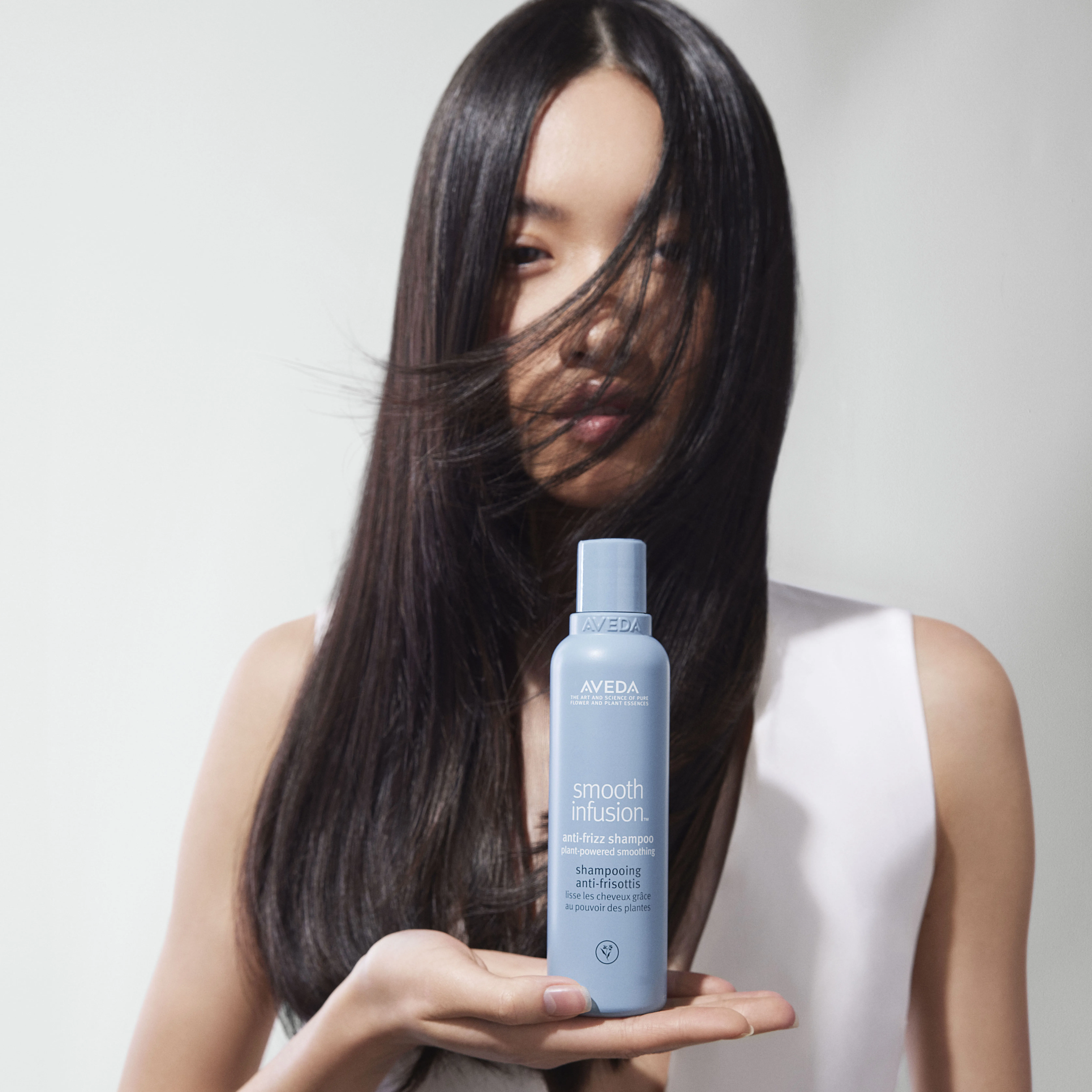 Frau mit langen glatten Haaren hält Aveda Smooth Infusion Shampoo