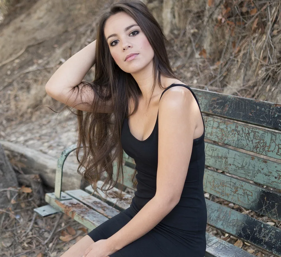 Frau mit dunkelbraunen langen Haaren sitzt auf Parkbank