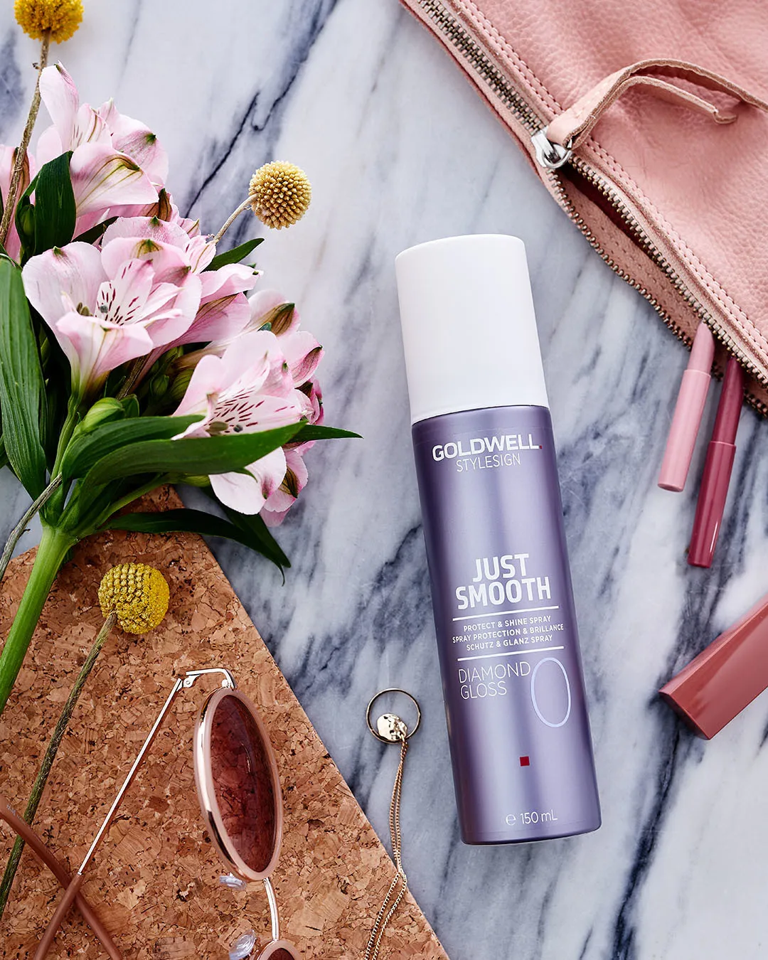 Goldwell Glanzspray auf Tische neben Blume, Brille und Kosmetiktasche